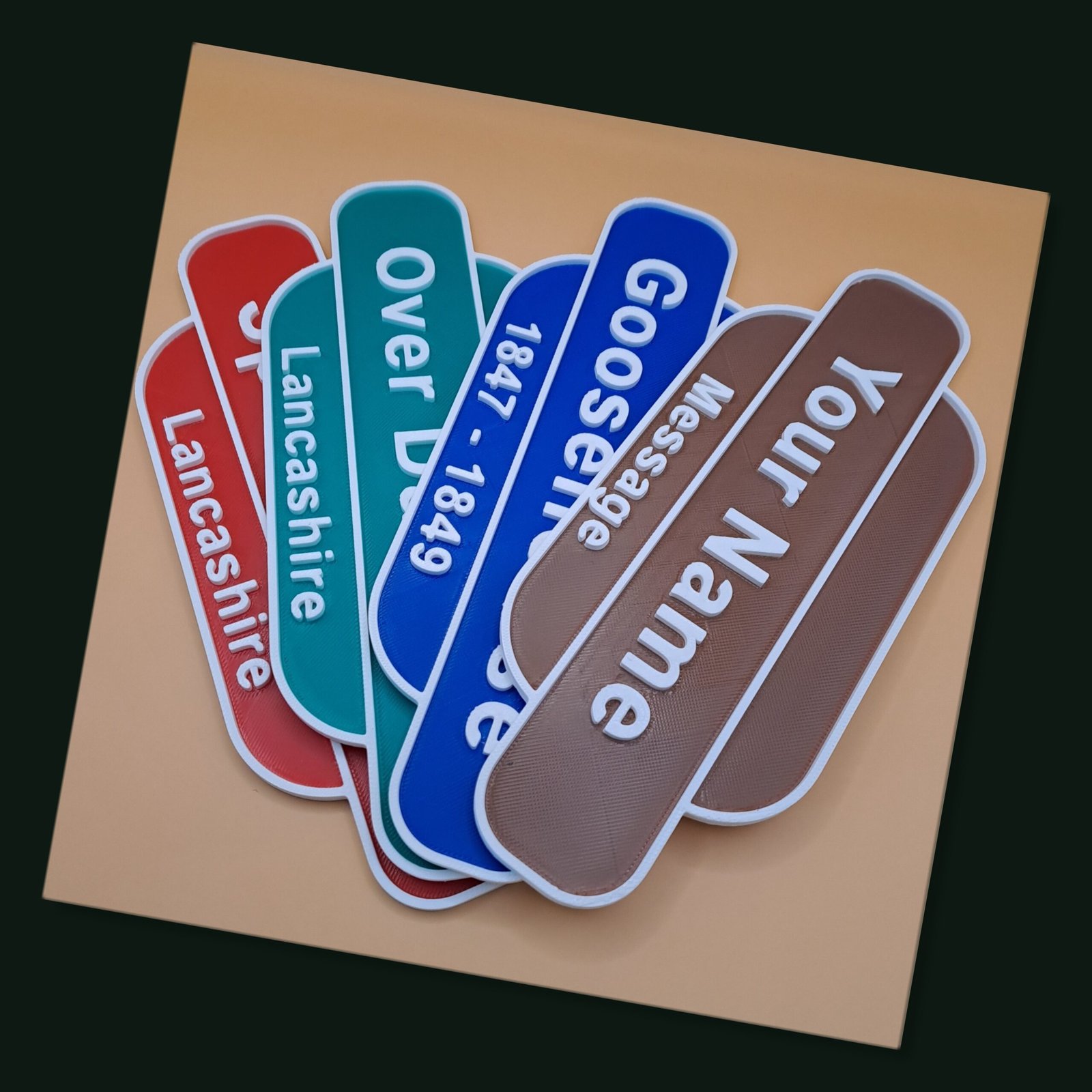 A collection of personalised 3D printed British Railways style station totem signs fan-spread in various colours including red, blue, green, and brown.